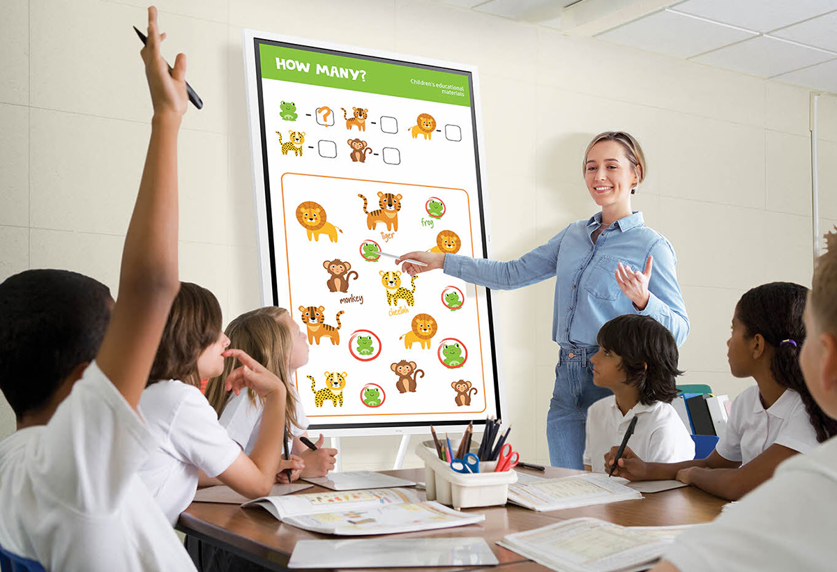 Απεικονίζεται δασκάλα να διδάσκει μικρά παιδιά με τη χρήση του digital signage.